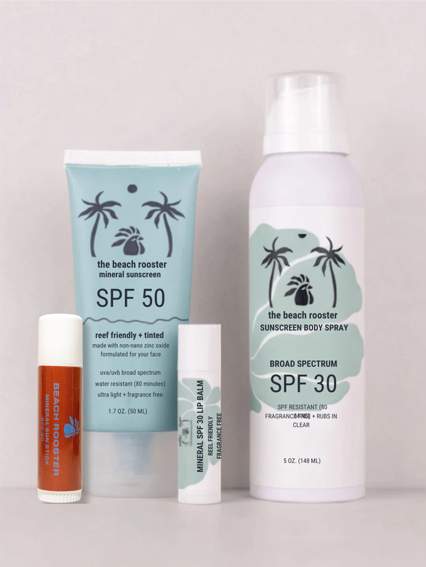 A sunscreen and lip care set from The Beach Rooster, including a light blue tube of mineral sunscreen SPF 50, a white bottle of broad spectrum sunscreen body spray SPF 30, and two lip products, arranged on a light gray background.