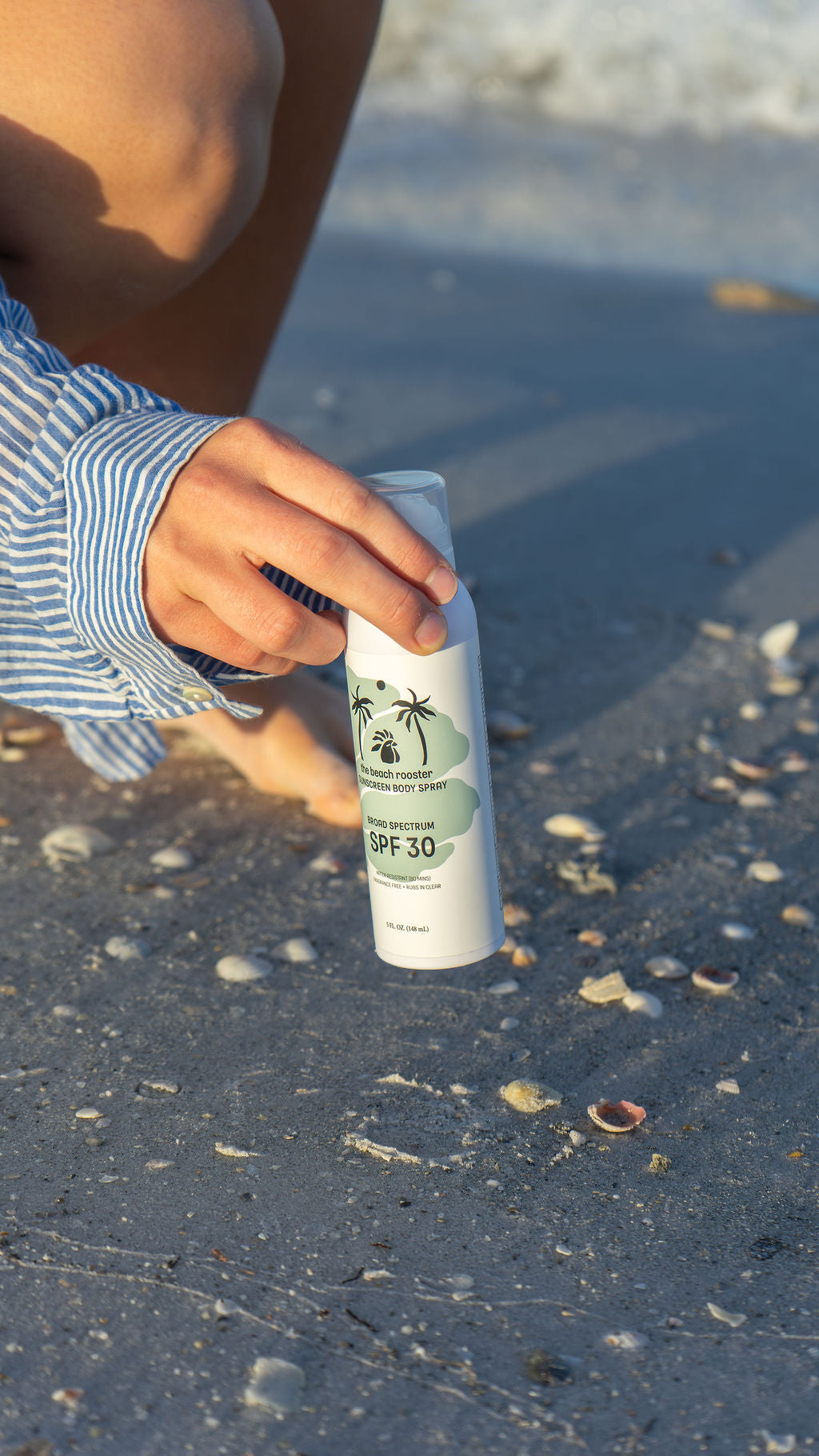 Woman holding The Beach Rooster SPF 30 Mineral Sunscreen Body Spray on a beach 