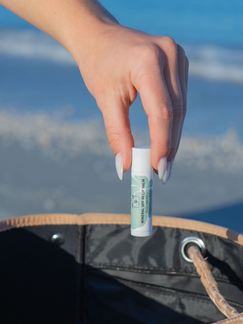 Person adding a SPF 30 mineral lip balm with The Beach Rooster brand label to their beach bag 