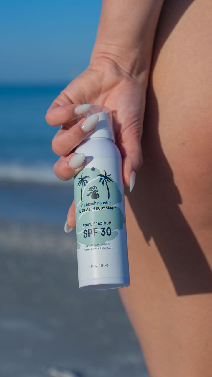 Woman holding The Beach Rooster SPF 30 Mineral Sunscreen Body Spray on a beach 