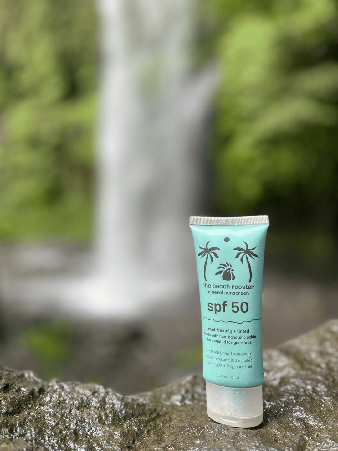 Tube of sunscreen with SPF 50 on a rock in front of a waterfall