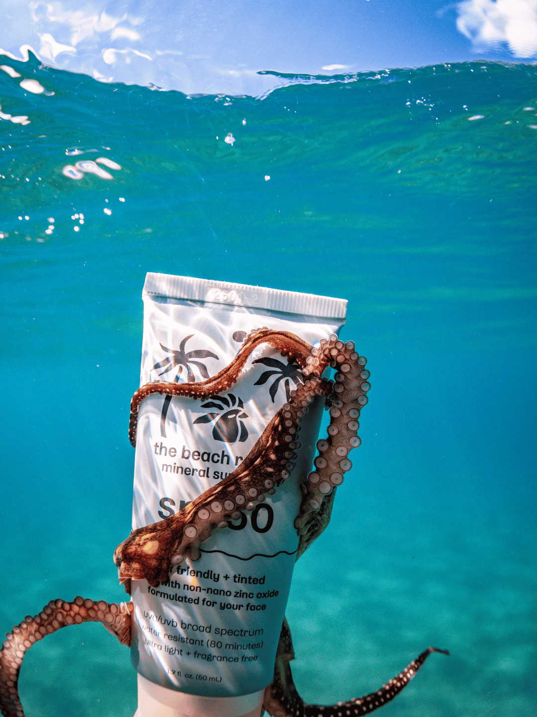 Tube of sunscreen with an octopus holding it underwater against a blue ocean background