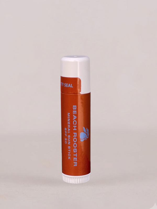 A single tube of lip balm standing upright on a plain light gray background. The tube is orange-brown with a white cap and base, and visible text includes 'BEACH ROOSTER' and 'LIP Balm'.