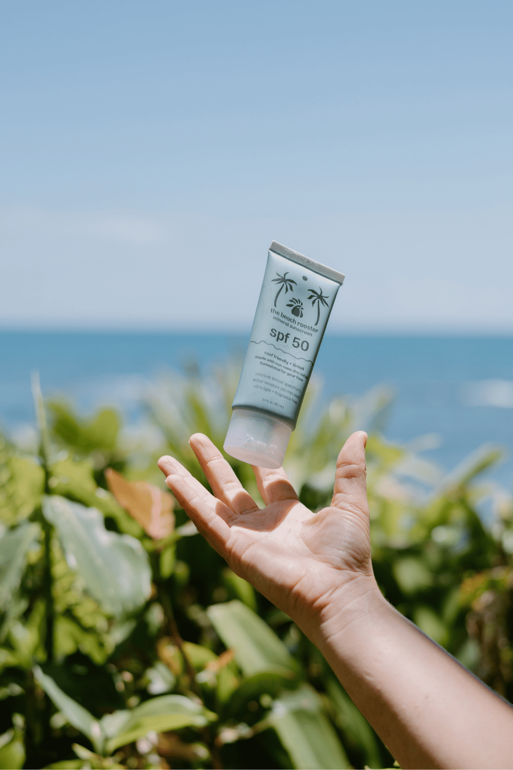 Tinted mineral sunscreen getting caught by a woman with a beach and ocean background 