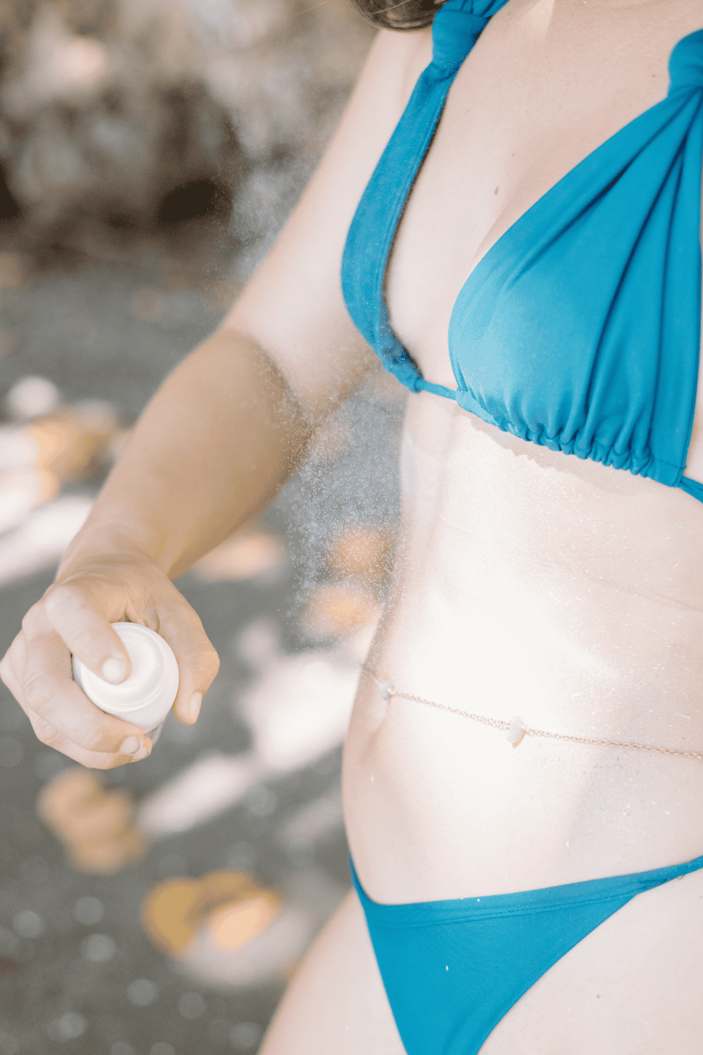woman using a mineral sunscreen spray in a blue bikini 